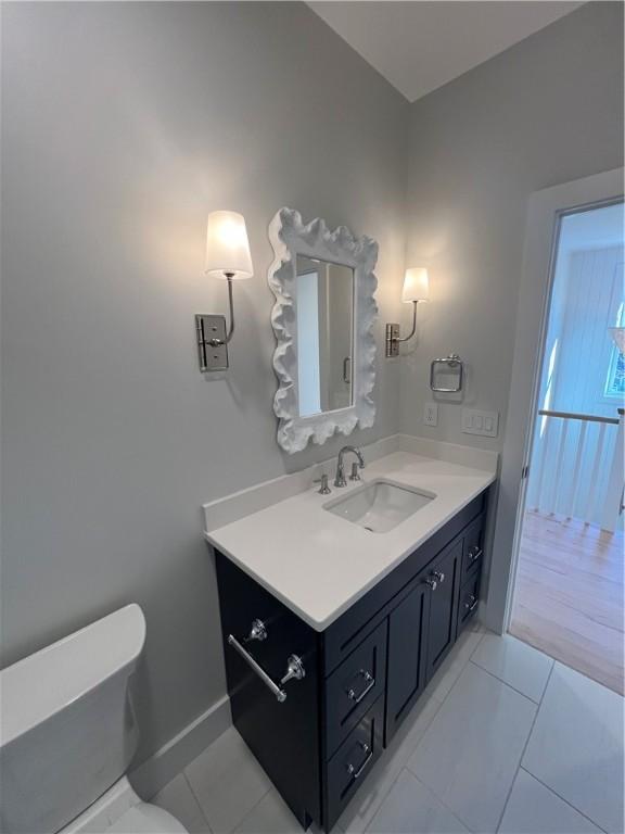 half bath with baseboards, vanity, toilet, and tile patterned floors