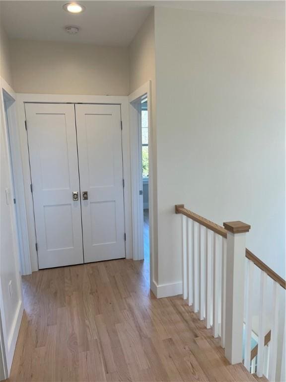 hallway with light wood-type flooring, baseboards, and an upstairs landing