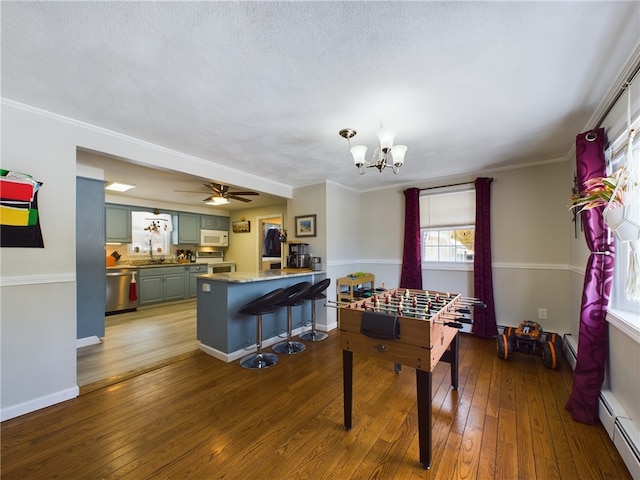 game room with a baseboard radiator, hardwood / wood-style flooring, ceiling fan with notable chandelier, baseboards, and ornamental molding