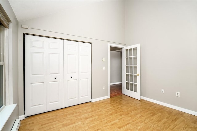 unfurnished bedroom with a closet, light wood-style flooring, a baseboard heating unit, vaulted ceiling, and baseboards