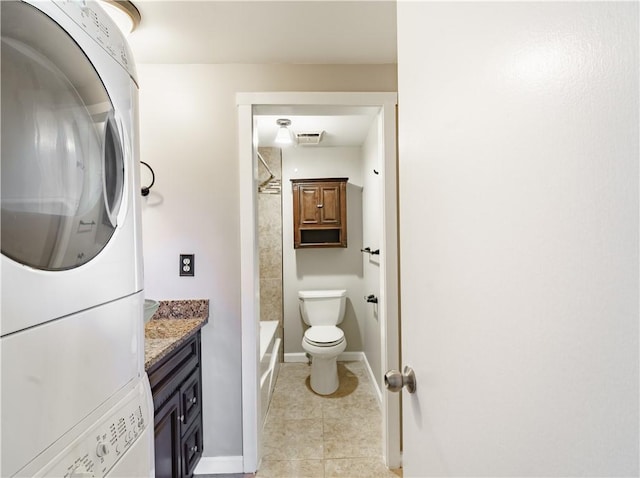 bathroom featuring toilet, stacked washer / dryer, vanity, tile patterned flooring, and baseboards