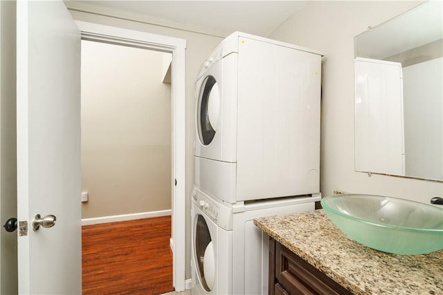 laundry room with laundry area, baseboards, stacked washer / dryer, wood finished floors, and a sink