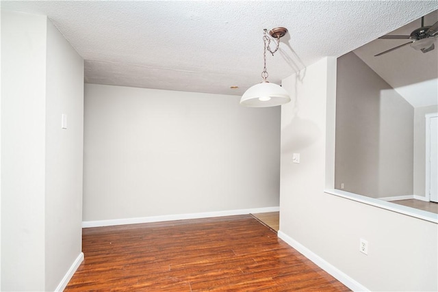 unfurnished dining area featuring ceiling fan, a textured ceiling, wood finished floors, and baseboards