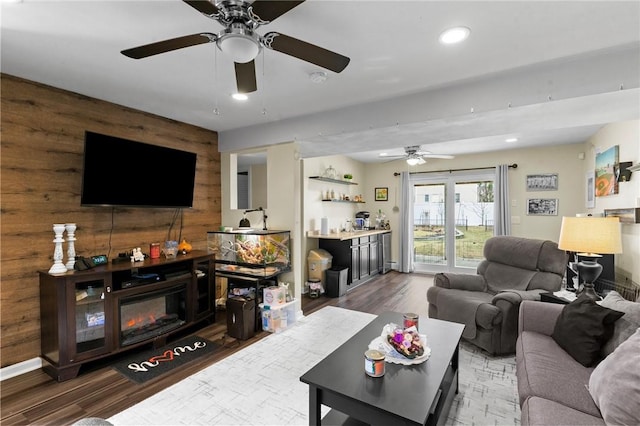 living area featuring recessed lighting, wood walls, wood finished floors, a bar, and a glass covered fireplace