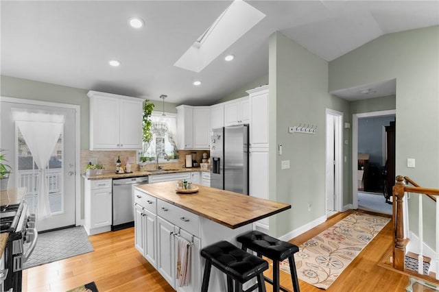 kitchen with light wood finished floors, appliances with stainless steel finishes, white cabinets, vaulted ceiling with skylight, and a kitchen bar