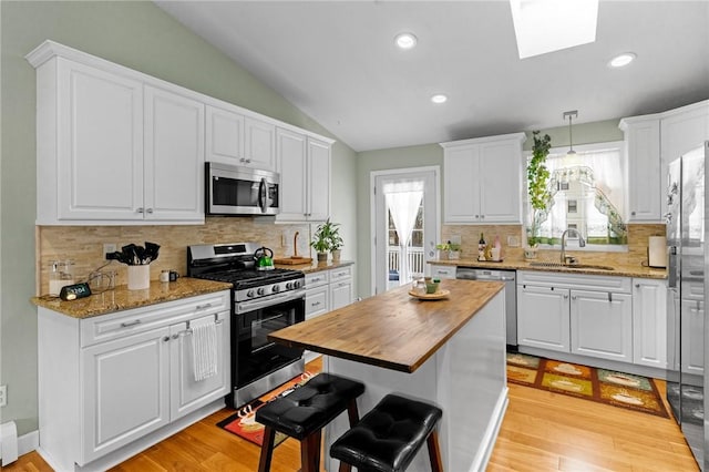 kitchen with vaulted ceiling with skylight, stainless steel appliances, butcher block countertops, a sink, and white cabinets