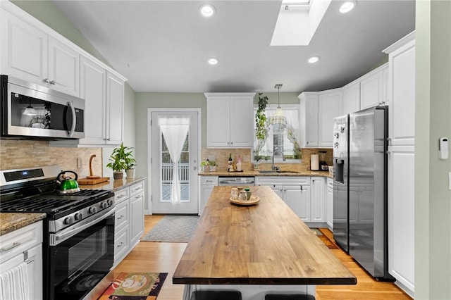 kitchen featuring a skylight, white cabinets, butcher block countertops, stainless steel appliances, and a sink