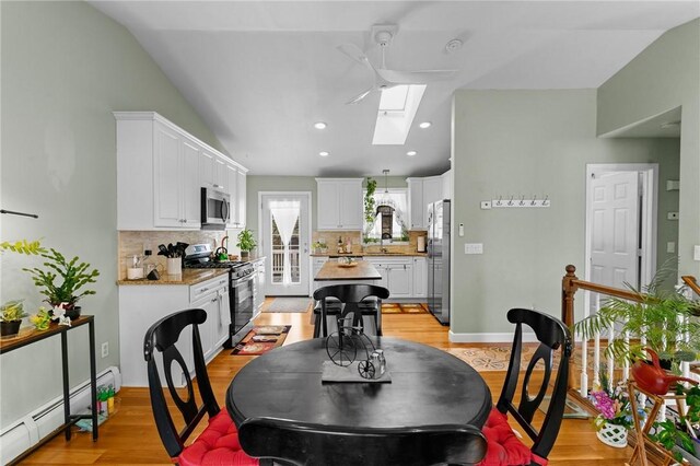 dining area with lofted ceiling with skylight, a baseboard radiator, light wood finished floors, and recessed lighting