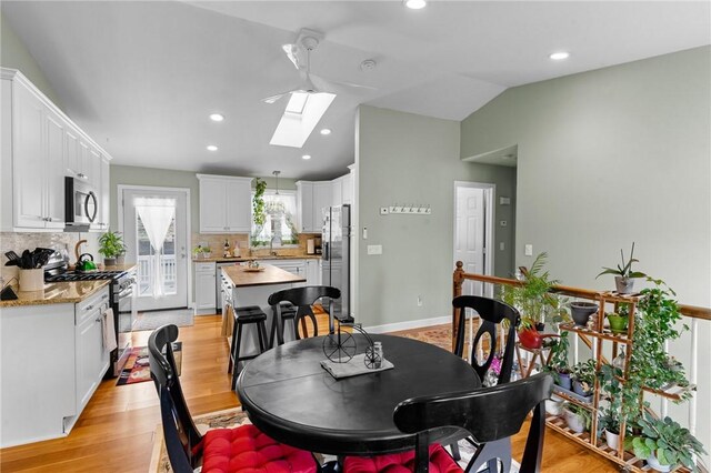 dining room featuring vaulted ceiling with skylight, baseboards, light wood-style flooring, and recessed lighting