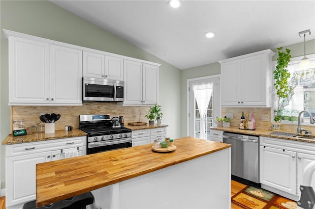 kitchen with a sink, a healthy amount of sunlight, vaulted ceiling, wooden counters, and appliances with stainless steel finishes