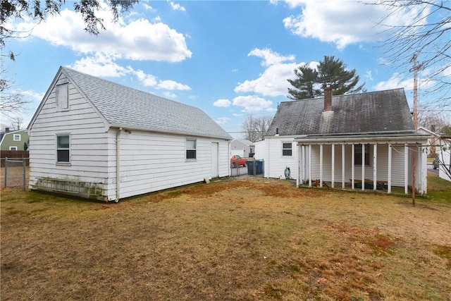 rear view of property with roof with shingles, a yard, a chimney, and fence