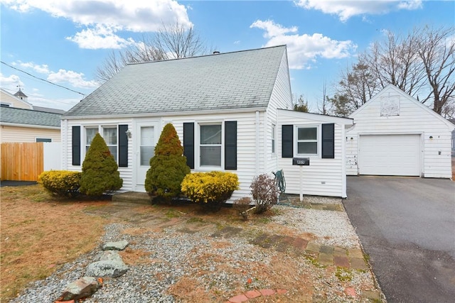 view of front of house featuring a garage, aphalt driveway, roof with shingles, fence, and an outdoor structure