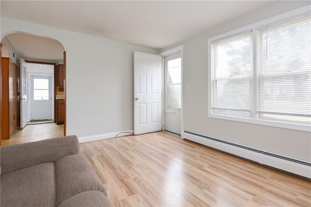 unfurnished living room with light wood finished floors, baseboards, arched walkways, and baseboard heating