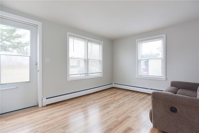 living area featuring light wood-style floors, a healthy amount of sunlight, and a baseboard heating unit