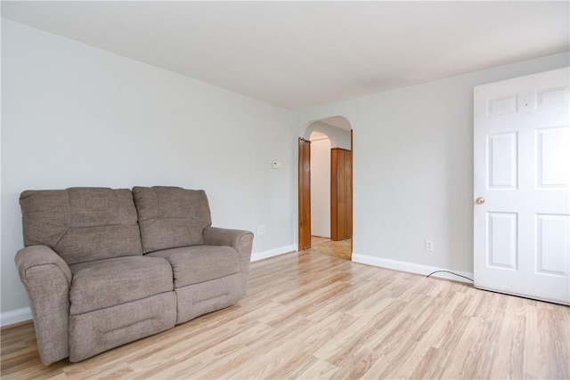 living area featuring arched walkways, light wood-style flooring, and baseboards