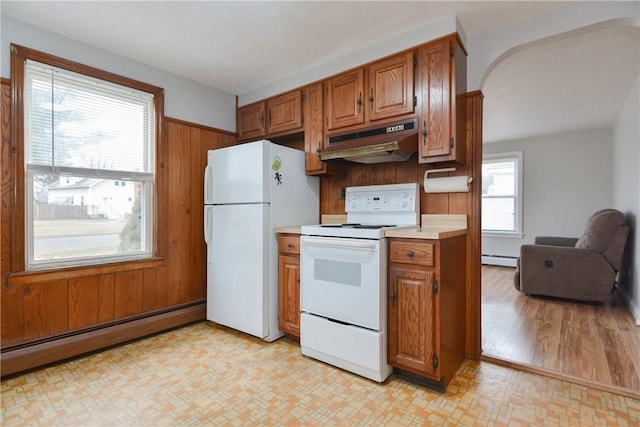 kitchen featuring brown cabinets, under cabinet range hood, a baseboard radiator, and white appliances