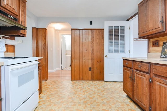 kitchen with arched walkways, under cabinet range hood, light countertops, light floors, and white electric range oven