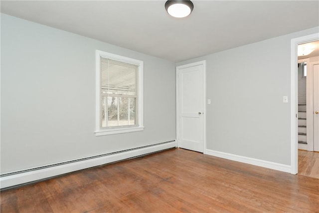 empty room with a baseboard heating unit, baseboards, and wood finished floors