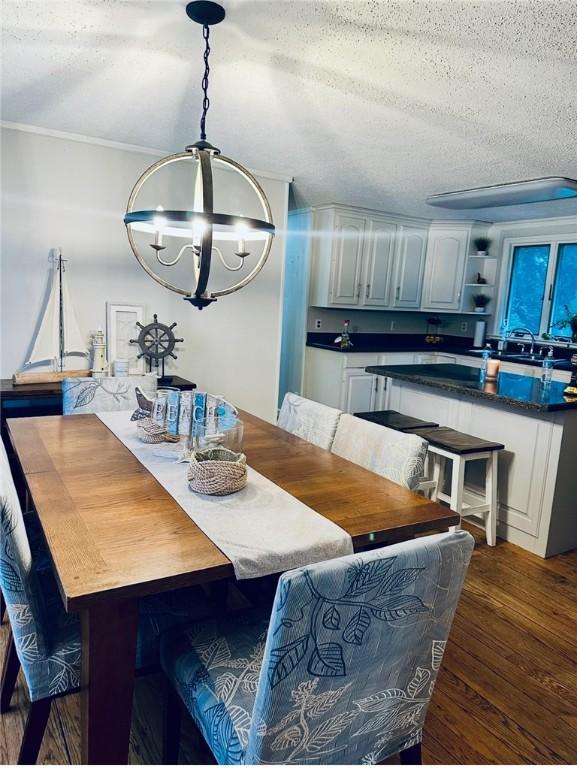 dining space with dark wood-type flooring, ornamental molding, a textured ceiling, and an inviting chandelier