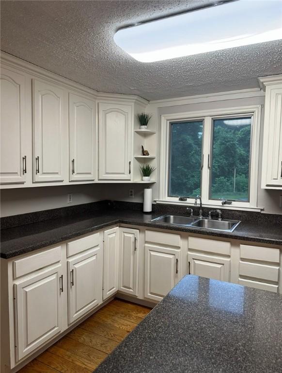 kitchen featuring a textured ceiling, dark wood-style flooring, a sink, white cabinetry, and dark countertops