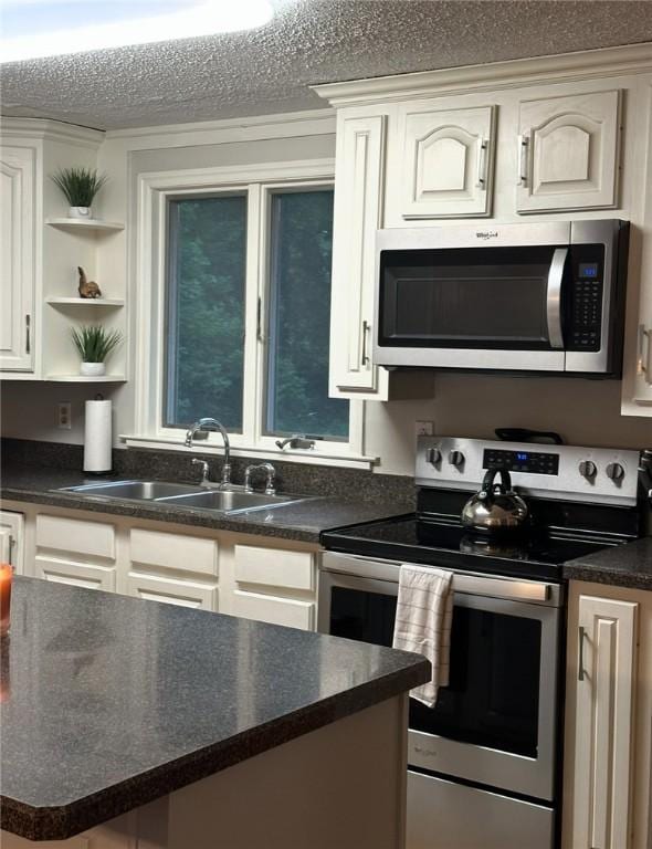 kitchen with open shelves, stainless steel appliances, dark countertops, a sink, and a textured ceiling