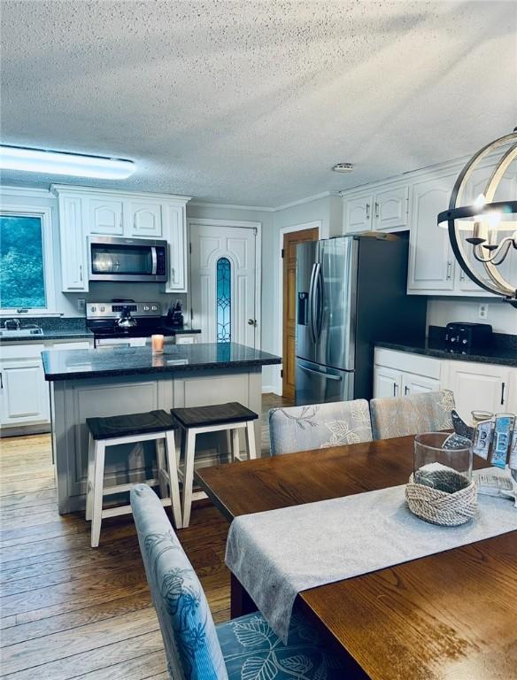 kitchen with a breakfast bar area, dark countertops, appliances with stainless steel finishes, white cabinetry, and light wood-type flooring