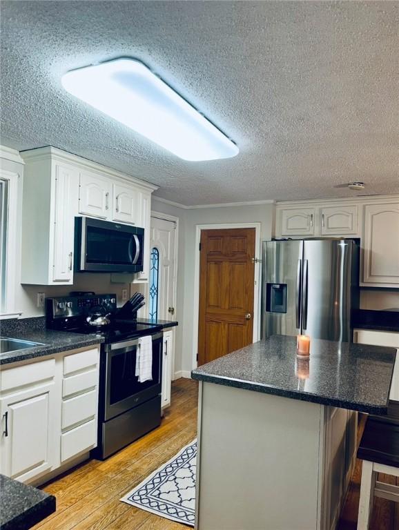 kitchen with light wood finished floors, a breakfast bar area, stainless steel appliances, a textured ceiling, and white cabinetry