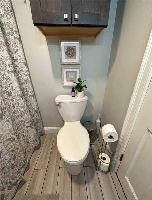 bathroom featuring wood finish floors, a shower with curtain, toilet, and baseboards