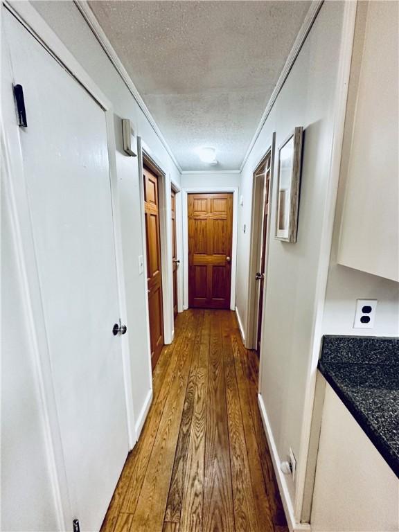 hallway with ornamental molding, a textured ceiling, baseboards, and wood finished floors