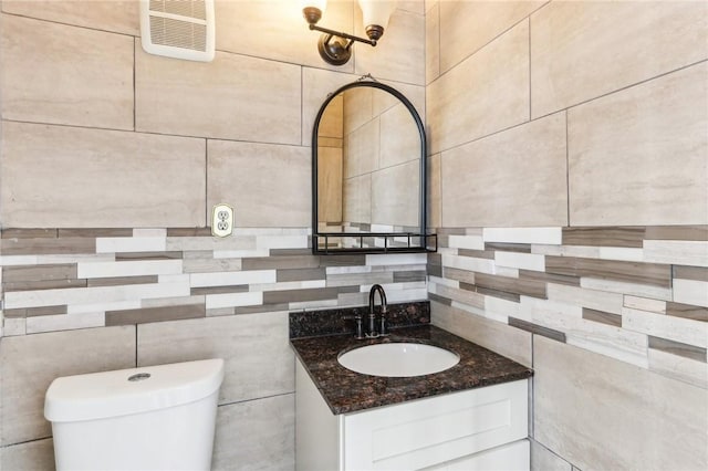 half bathroom featuring vanity, tile walls, toilet, and visible vents