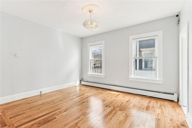 spare room with a chandelier, light wood-type flooring, baseboards, and a baseboard radiator