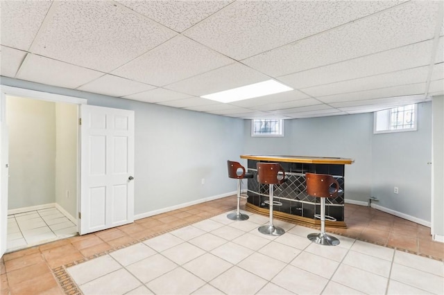 bar featuring tile patterned floors, baseboards, a paneled ceiling, and a bar