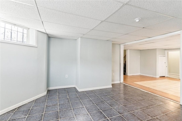 basement featuring dark tile patterned floors, baseboards, and a drop ceiling