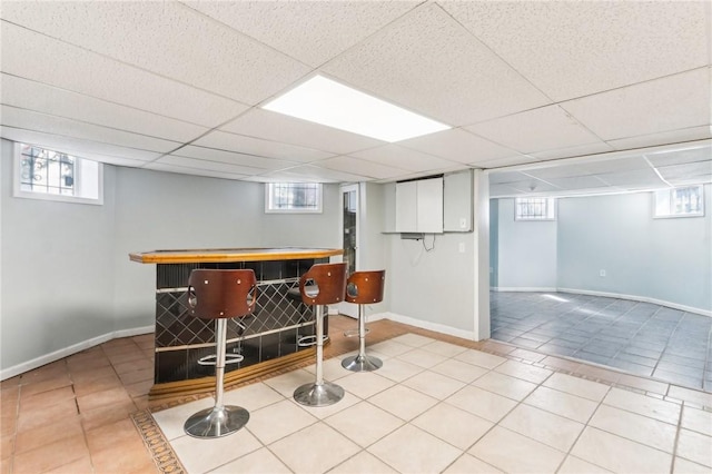 bar featuring a wealth of natural light, baseboards, a bar, and tile patterned flooring