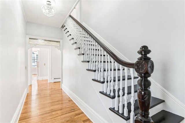 stairway featuring a baseboard radiator, baseboards, wood finished floors, and a chandelier