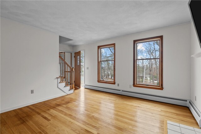 unfurnished room with a baseboard heating unit, stairway, light wood-type flooring, and baseboards