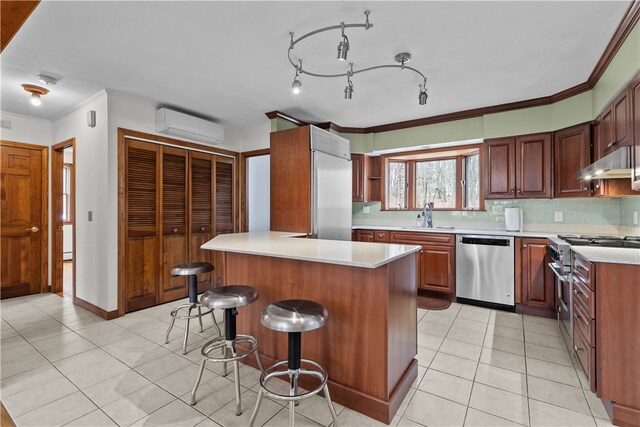 kitchen featuring premium appliances, a wall mounted AC, a sink, under cabinet range hood, and a kitchen breakfast bar