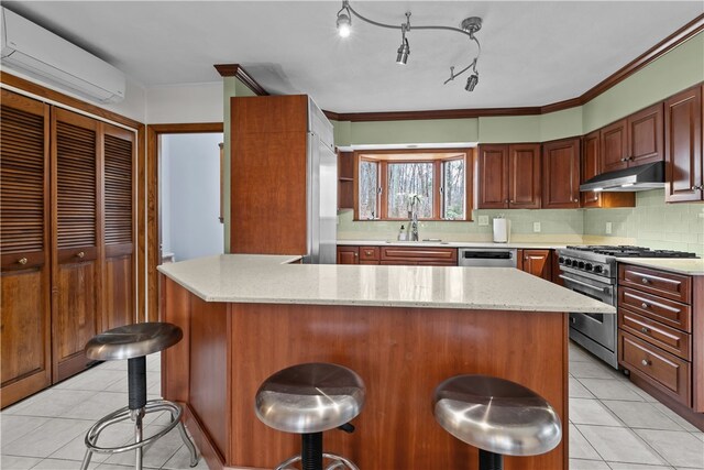 kitchen featuring a wall mounted air conditioner, stainless steel appliances, under cabinet range hood, a kitchen bar, and a sink