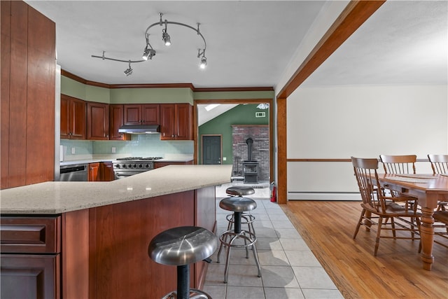 kitchen featuring decorative backsplash, a baseboard radiator, a wood stove, stainless steel appliances, and under cabinet range hood