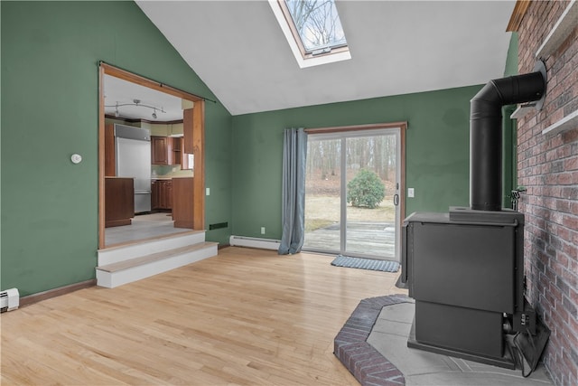 living room featuring light wood-style flooring, a baseboard heating unit, a wood stove, vaulted ceiling with skylight, and baseboards