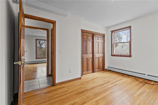 unfurnished bedroom with a baseboard radiator, baseboards, light wood-style floors, baseboard heating, and a closet