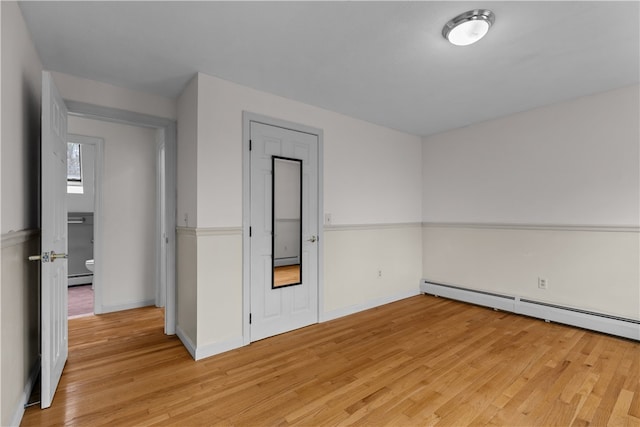 spare room featuring light wood-style floors, a baseboard radiator, and baseboards