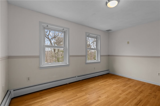 spare room featuring light wood-type flooring, visible vents, a baseboard heating unit, and baseboards