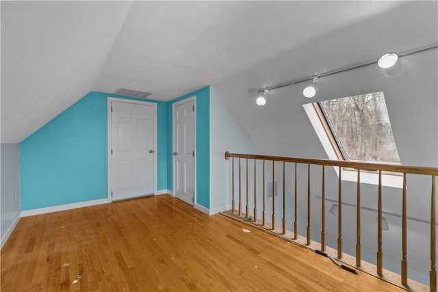 additional living space featuring vaulted ceiling with skylight, visible vents, baseboards, and hardwood / wood-style floors