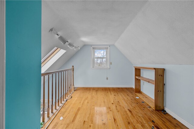 additional living space featuring lofted ceiling with skylight, a textured ceiling, baseboards, and hardwood / wood-style flooring