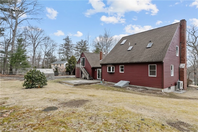 rear view of house featuring a shingled roof, a chimney, an outdoor structure, and fence