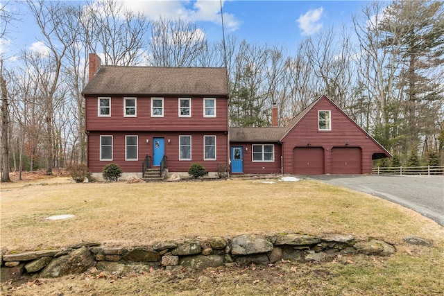 colonial house with aphalt driveway, a front yard, fence, and a chimney