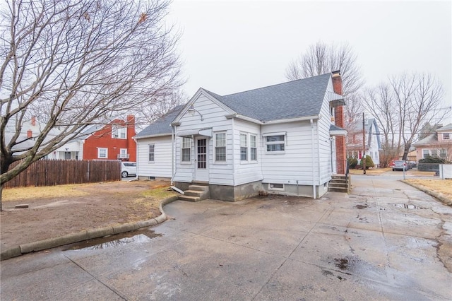 view of front facade featuring entry steps, a shingled roof, concrete driveway, a chimney, and fence