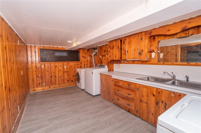 washroom featuring laundry area, wooden walls, washer and dryer, light wood-style floors, and a sink