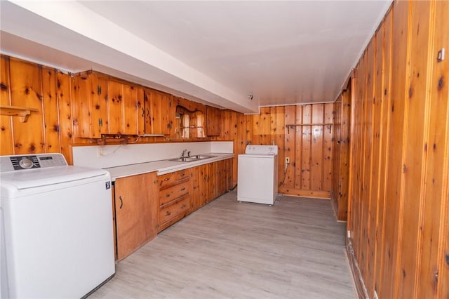 laundry area with light wood-type flooring, washer / clothes dryer, a sink, and wooden walls